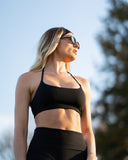 Woman in black athletic wear standing outdoors with a blurred natural background
