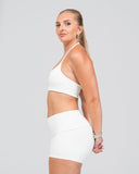 Woman wearing a white sports bra and shorts on a plain background