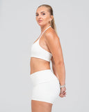 Woman wearing a white sports bra and shorts on a plain background